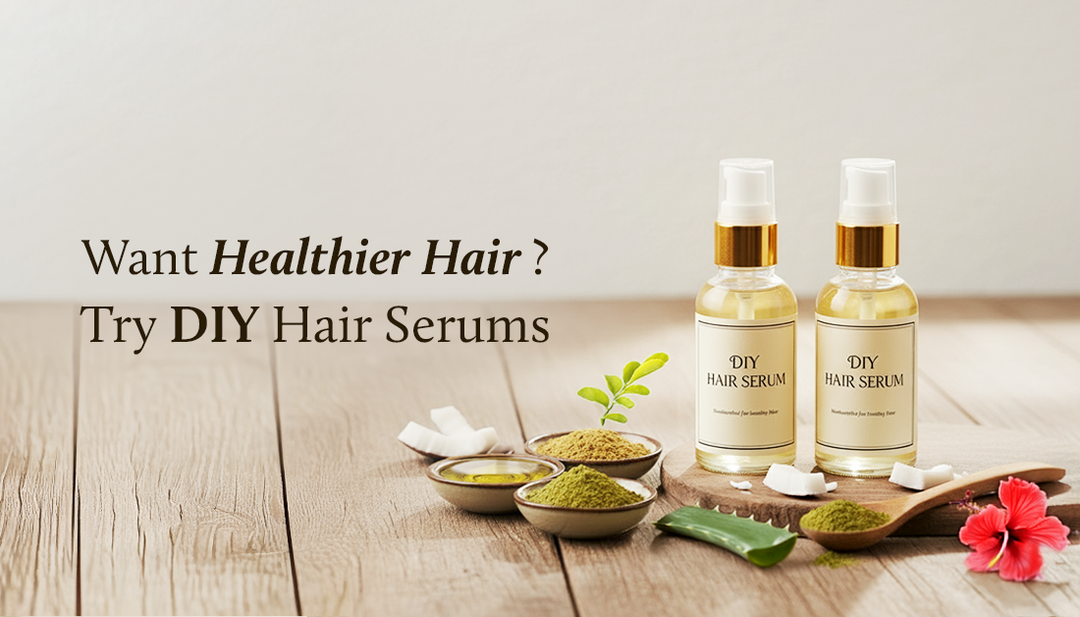 Two hair serum bottles surrounded by natural ingredients like aloe vera, a bowl of powder, hibiscus flowers, and curry leaves, all placed on a wooden table