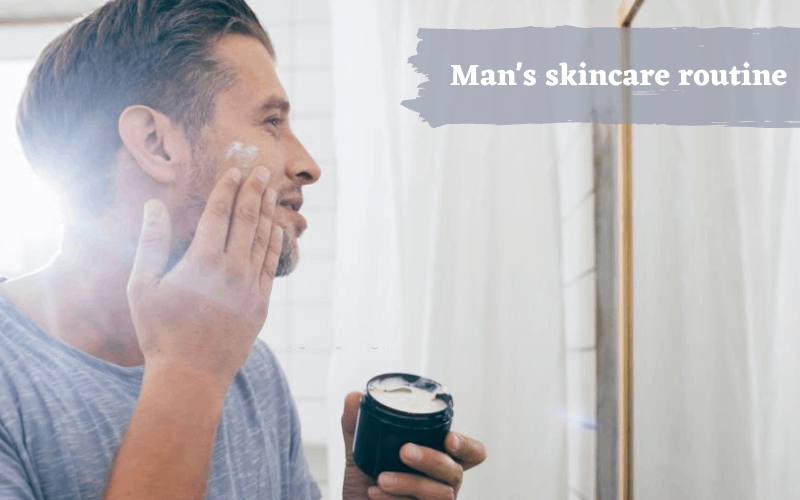 Man is standing infront of mirror and applying face cream on his cheeks 