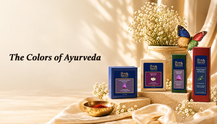 The text- “Colors of Ayurveda” display with Blue Nectar product boxes, white flowers, a brass bowl, soft draped fabric, and a colorful butterfly; serene, warm tone.