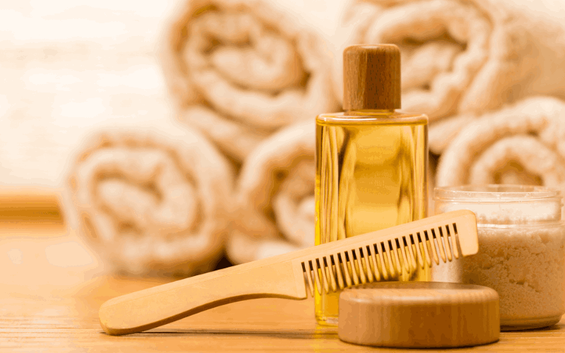 Bhringraj oil bottle with wooden comb is placed on table with towels at the background