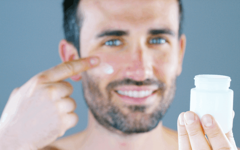 Men is applying kumkumadi cream on his right cheek and holding the cream box from his left hand 