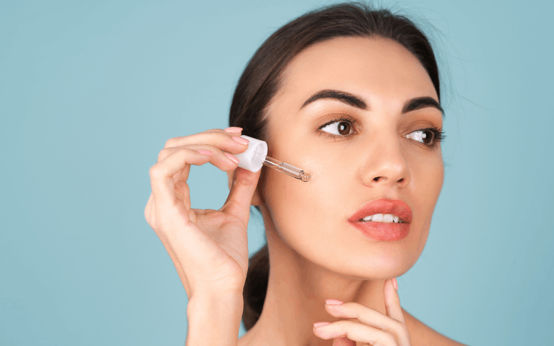 Girl is applying kumkumadi serum by applicator on her cheeks 