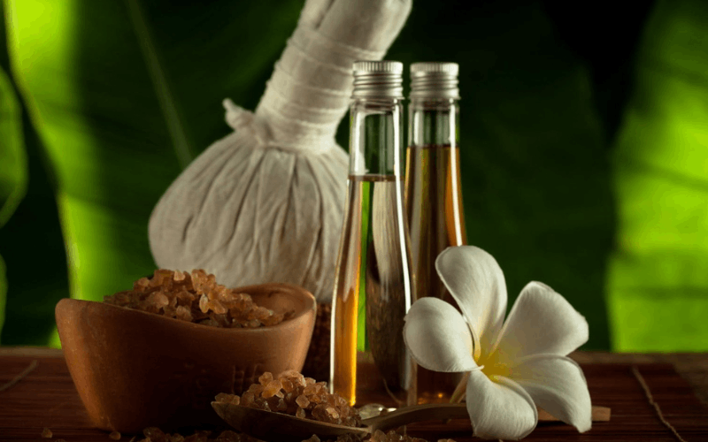 two pain oil bottles, white flower, potli and ayurvedic ingredients in bowl on table
