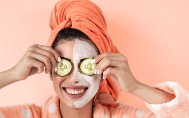 lady has applied face pack for glowing skin and holding cucumber infront of eyes