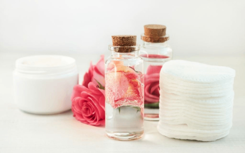 Rose water and cotton pads for face with roses are on table 